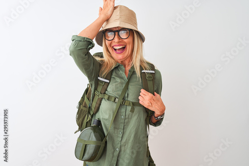 Middle age hiker woman wearing backpack hat canteen glasses over isolated white background surprised with hand on head for mistake  remember error. Forgot  bad memory concept.