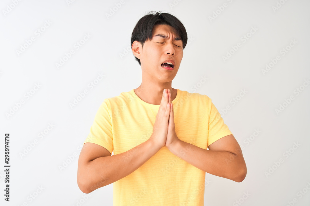Chinese man wearing yellow casual t-shirt standing over isolated white background begging and praying with hands together with hope expression on face very emotional and worried. Chinese man wearing yellow casual t-shirt standing over isolated white background begging and praying with hands together with hope expression on face very emotional and worried.
