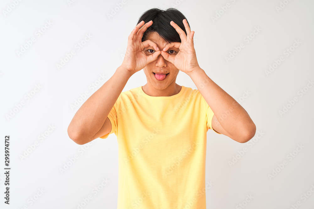 Chinese man wearing yellow casual t-shirt standing over isolated white background doing ok gesture like binoculars sticking tongue out, eyes looking through fingers. Crazy expression. Chinese man wearing yellow casual t-shirt standing over isolated white background doing ok gesture like binoculars sticking tongue out, eyes looking through fingers. Crazy expression.