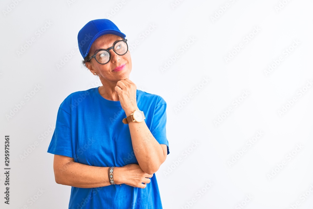 Senior deliverywoman wearing cap and glasses standing over isolated white background with hand on chin thinking about question, pensive expression. Smiling with thoughtful face. Doubt concept. Senior deliverywoman wearing cap and glasses standing over isolated white background with hand on chin thinking about question, pensive expression. Smiling with thoughtful face. Doubt concept.
