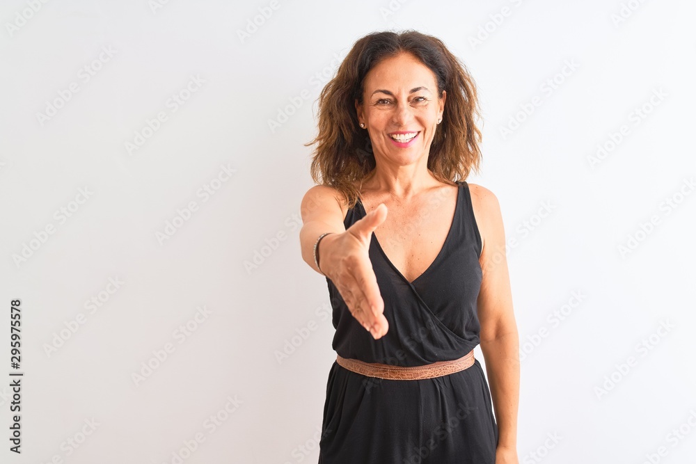 Middle age woman wearing black casual dress standing over isolated white background smiling friendly offering handshake as greeting and welcoming. Successful business. Middle age woman wearing black casual dress standing over isolated white background smiling friendly offering handshake as greeting and welcoming. Successful business.