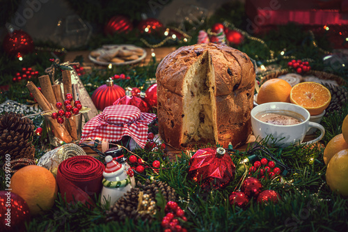 Christmas ingredients table with a Panettone in the center on a wooden board, accompanied by hot chocoalte, orange, cookies, cinnamon, pine.