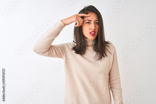Beautiful chinese woman wearing turtleneck sweater standing over isolated white background pointing unhappy to pimple on forehead, ugly infection of blackhead. Acne and skin problem