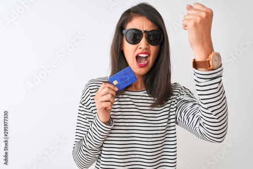 Young chinese woman wearing sunglasses holding credit card over isolated white background annoyed and frustrated shouting with anger, crazy and yelling with raised hand, anger concept