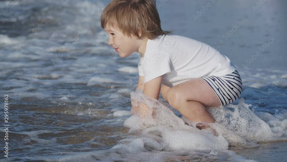Toddler boy in swimwear is playing with sand on sea side. Toddler boy in swimwear is playing with sand on sea side.