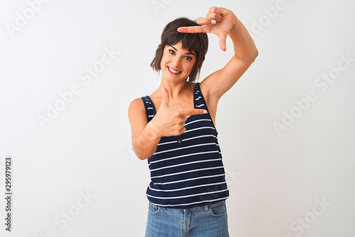 Young beautiful woman wearing striped t-shirt standing over isolated white background smiling making frame with hands and fingers with happy face. Creativity and photography concept.