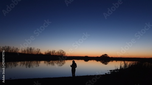silhouette of woman on lake at sunset