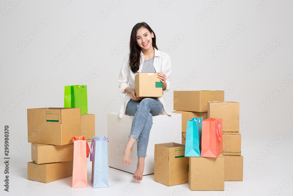 Young woman freelancer working and checklist and writing order with cardboard box on white background - SME business online and delivery concept Young woman freelancer working and checklist and writing order with cardboard box on white background - SME business online and delivery concept