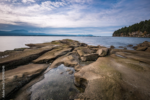 sand stone with unique formation in the cove under cloudy sky near dusk with forest covered island edge on the side