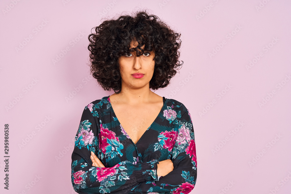 Young arab woman with curly hair wearing floral dress over isolated pink background skeptic and nervous, disapproving expression on face with crossed arms. Negative person. Young arab woman with curly hair wearing floral dress over isolated pink background skeptic and nervous, disapproving expression on face with crossed arms. Negative person.