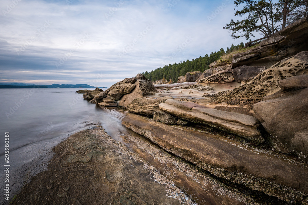 sand stone with unique formation in the cove under cloudy sky near dusk with forest covered island edge on the side