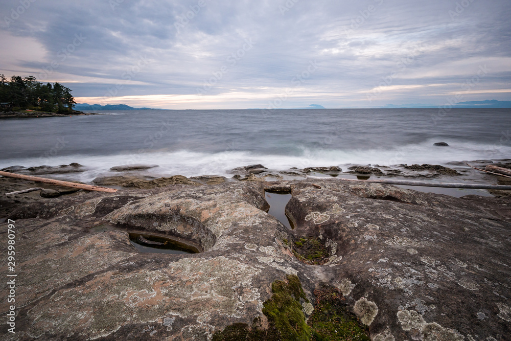 rocky coast line filled with sand stone by the ocean under cloudy sky near dusk 