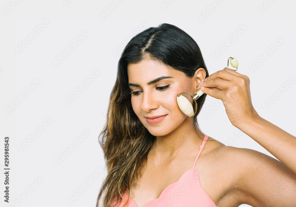 Beautiful Indian woman uses jade roller to massage her face Beautiful Indian woman uses jade roller to massage her face