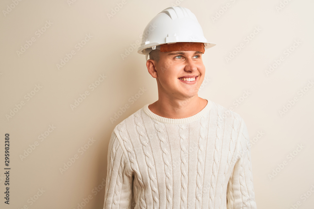 Handsome architect man wearing security helmet standing over isolated white background looking away to side with smile on face, natural expression. Laughing confident. Handsome architect man wearing security helmet standing over isolated white background looking away to side with smile on face, natural expression. Laughing confident.