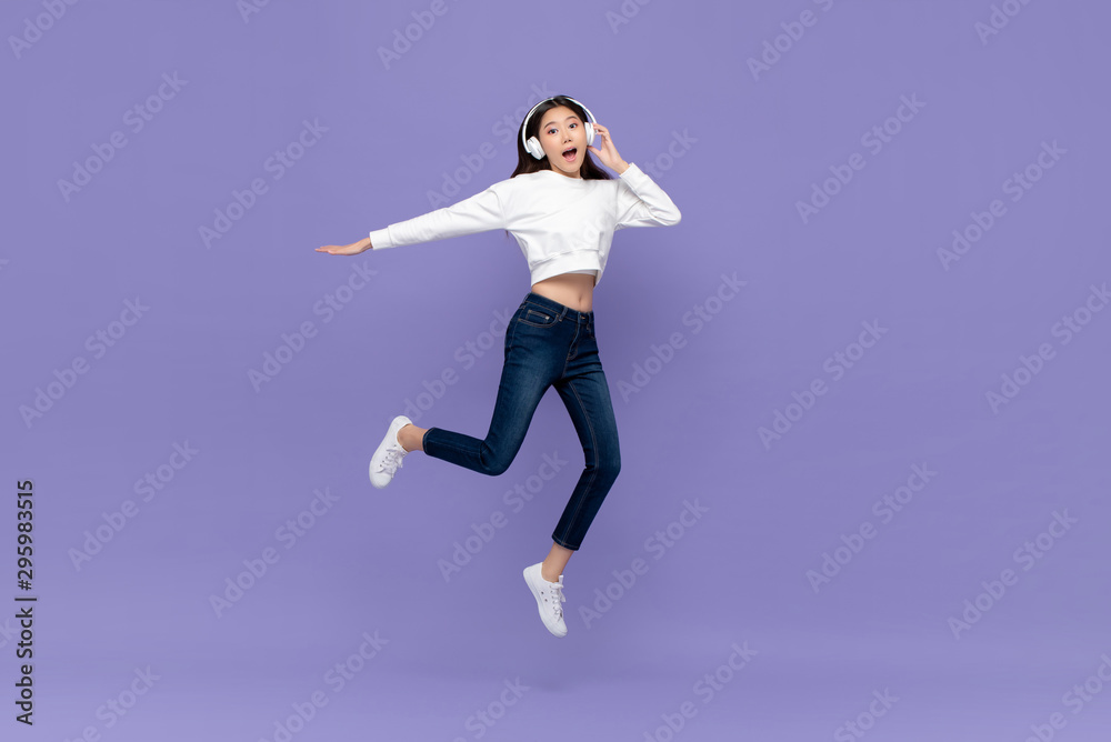 Asian woman jumping and listening to music on headphones