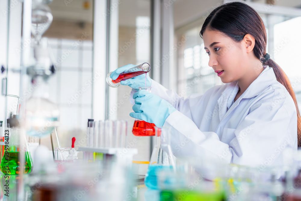 Attractive scientist woman looking chemical sample in flask at laboratory with lab glassware background. Science or chemistry research and development concept.