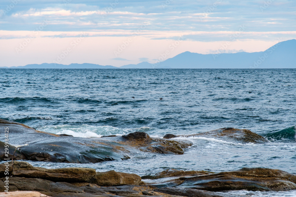 waves pounding the rocky shore line on a windy morning on the coast with mountain range over the horizon