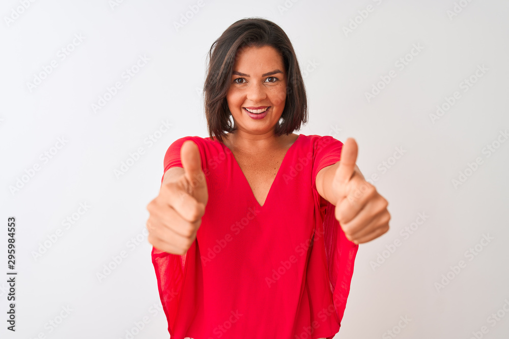 Young beautiful woman wearing red t-shirt standing over isolated white background doing happy thumbs up gesture with hand. Approving expression looking at the camera with showing success. Young beautiful woman wearing red t-shirt standing over isolated white background doing happy thumbs up gesture with hand. Approving expression looking at the camera with showing success.