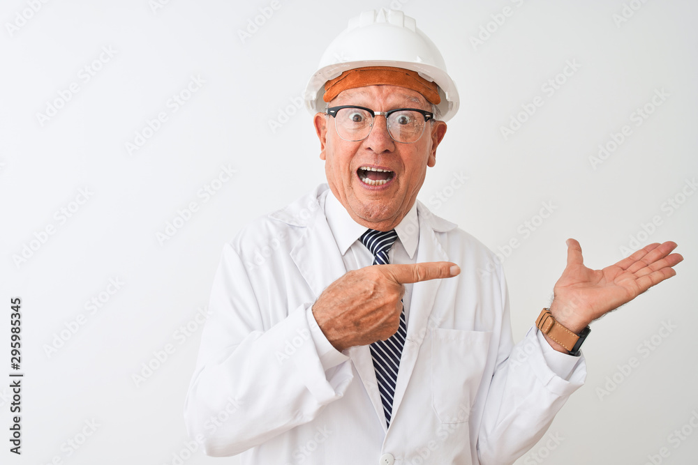 Senior grey-haired engineer man wearing coat and helmet over isolated white background amazed and smiling to the camera while presenting with hand and pointing with finger. Senior grey-haired engineer man wearing coat and helmet over isolated white background amazed and smiling to the camera while presenting with hand and pointing with finger.
