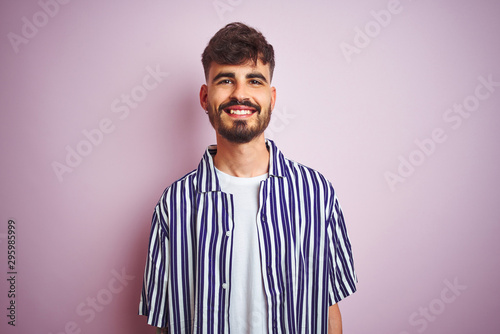 Young man with tattoo wearing striped shirt standing over isolated pink background with a happy and cool smile on face. Lucky person.