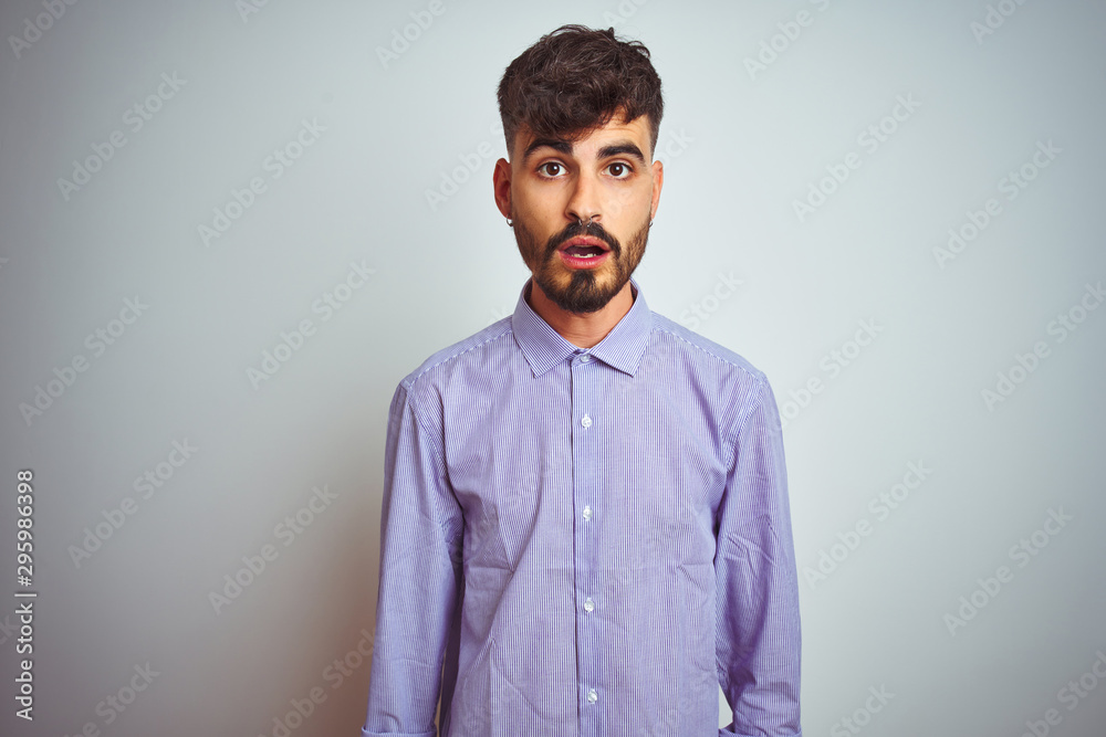 Young man with tattoo wearing purple shirt standing over isolated white background afraid and shocked with surprise expression, fear and excited face. Young man with tattoo wearing purple shirt standing over isolated white background afraid and shocked with surprise expression, fear and excited face.