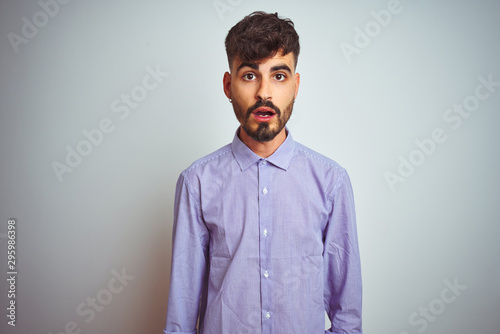 Young man with tattoo wearing purple shirt standing over isolated white background afraid and shocked with surprise expression, fear and excited face.