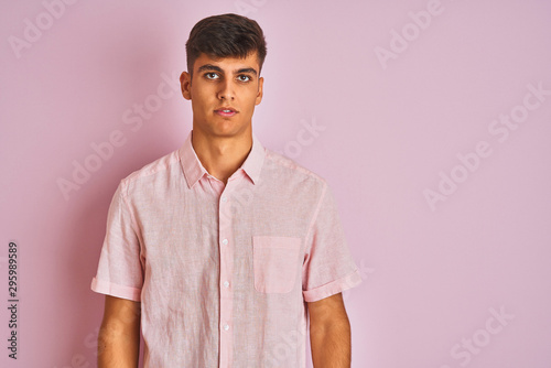 Young indian man wearing casual shirt standing over isolated pink background with serious expression on face. Simple and natural looking at the camera.