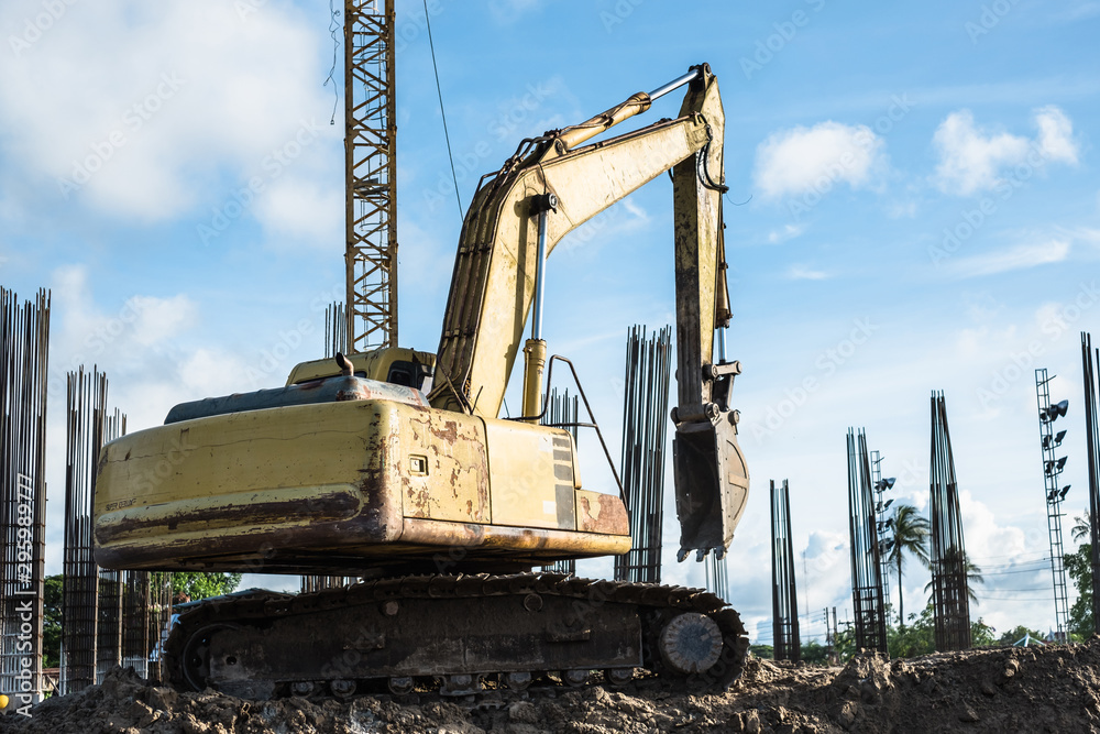 Old yellow backhoe or excavator work digging soil at new building construction site with steel concrete pillars in the back. Old yellow backhoe or excavator work digging soil at new building construction site with steel concrete pillars in the back.
