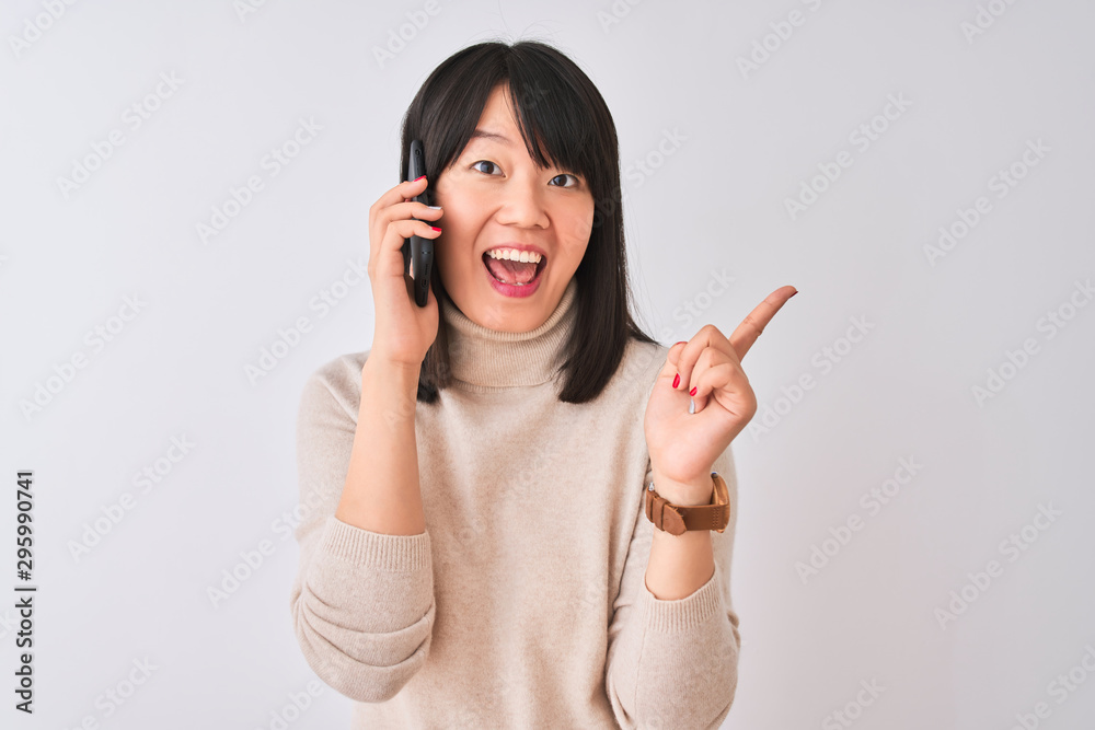 Young beautiful Chinese woman talking on the smartphone over isolated white background very happy pointing with hand and finger to the side Young beautiful Chinese woman talking on the smartphone over isolated white background very happy pointing with hand and finger to the side