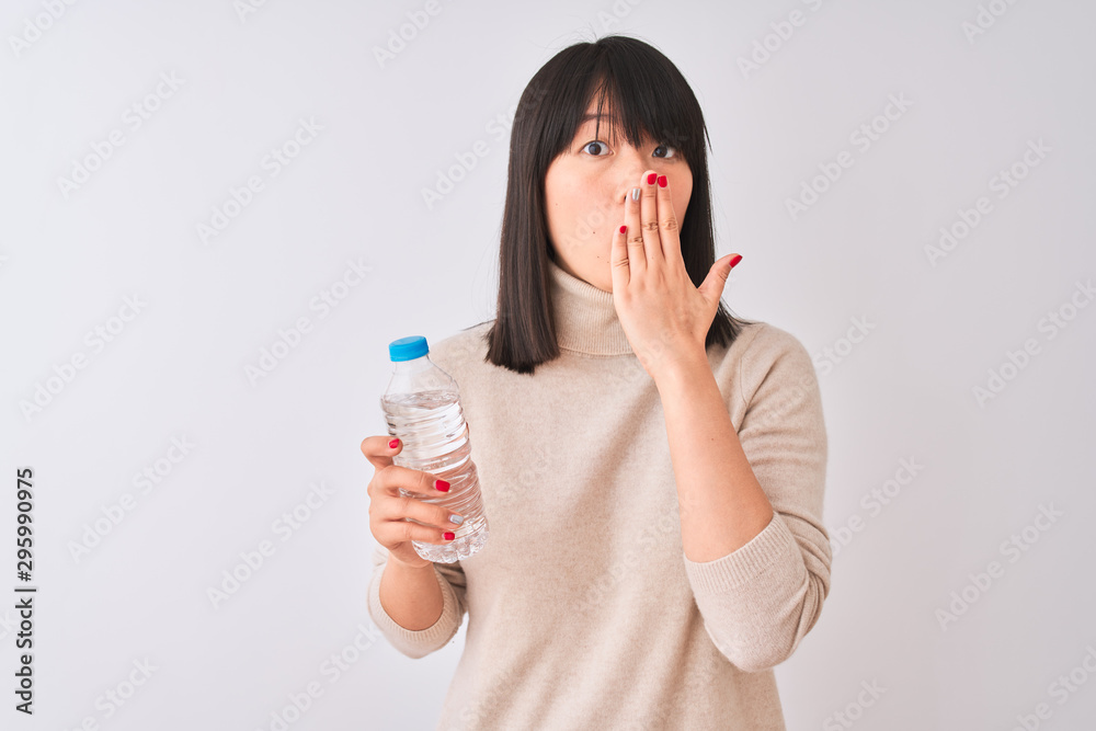 Young beautiful Chinese woman holding bottle of water over isolated white background cover mouth with hand shocked with shame for mistake, expression of fear, scared in silence, secret concept Young beautiful Chinese woman holding bottle of water over isolated white background cover mouth with hand shocked with shame for mistake, expression of fear, scared in silence, secret concept