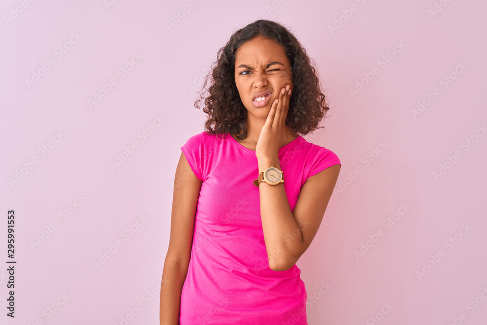 Young brazilian woman wearing t-shirt standing over isolated pink background touching mouth with hand with painful expression because of toothache or dental illness on teeth. Dentist concept. Young brazilian woman wearing t-shirt standing over isolated pink background touching mouth with hand with painful expression because of toothache or dental illness on teeth. Dentist concept.