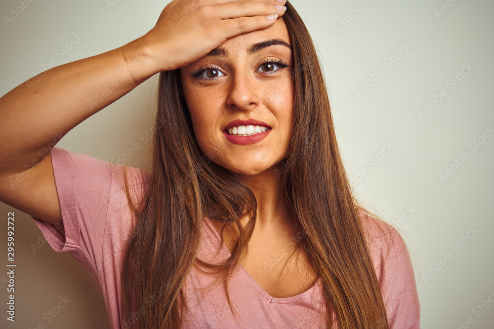 Fototapeta premium Young beautiful woman wearing pink t-shirt standing over isolated white background stressed with hand on head, shocked with shame and surprise face, angry and frustrated. Fear and upset for mistake.