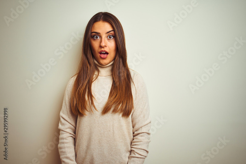 Young beautiful woman wearing winter turtleneck sweater over isolated white background afraid and shocked with surprise expression, fear and excited face.