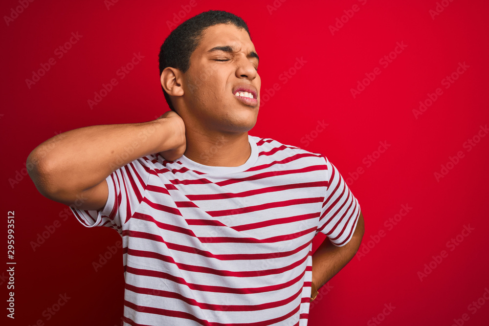 Young handsome arab man wearing striped t-shirt over isolated red background Suffering of neck ache injury, touching neck with hand, muscular pain Young handsome arab man wearing striped t-shirt over isolated red background Suffering of neck ache injury, touching neck with hand, muscular pain