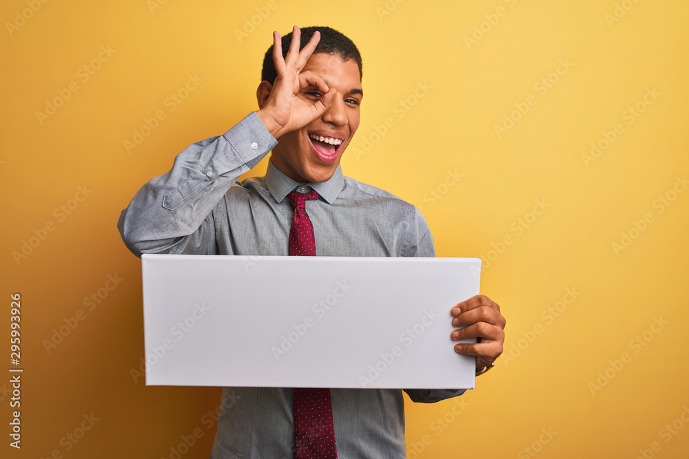 Young handsome arab businessman holding banner standing over isolated yellow background with happy face smiling doing ok sign with hand on eye looking through fingers Young handsome arab businessman holding banner standing over isolated yellow background with happy face smiling doing ok sign with hand on eye looking through fingers