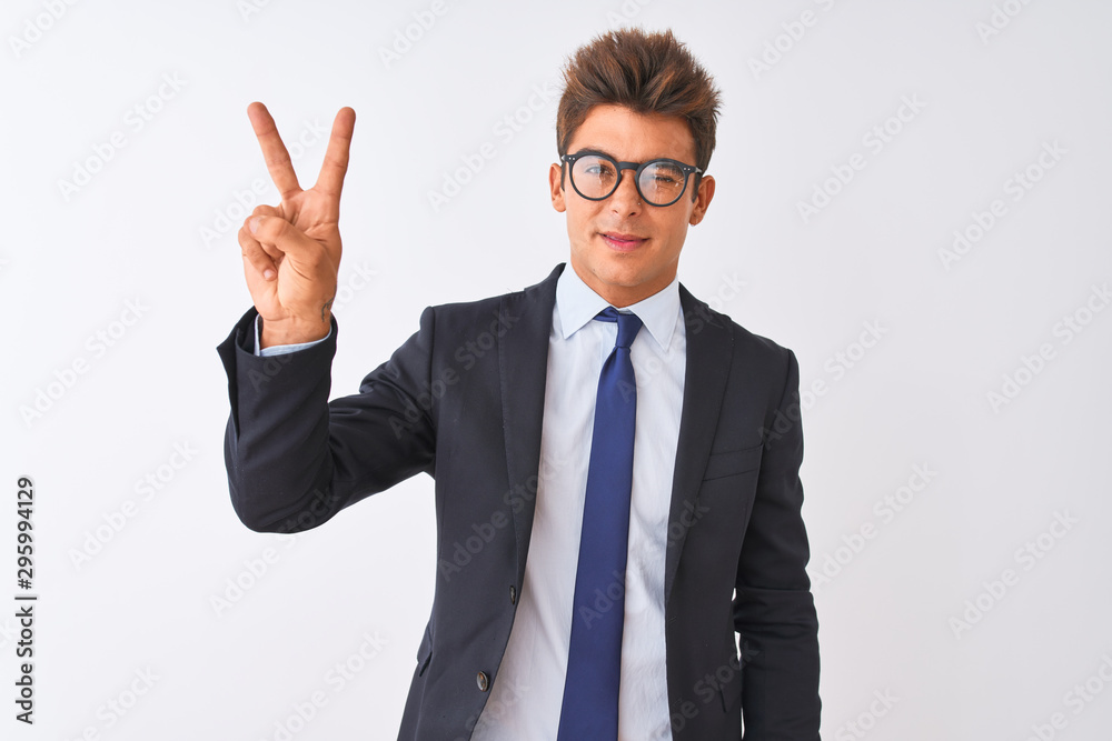 Young handsome businessman wearing suit and glasses over isolated white background smiling with happy face winking at the camera doing victory sign. Number two.