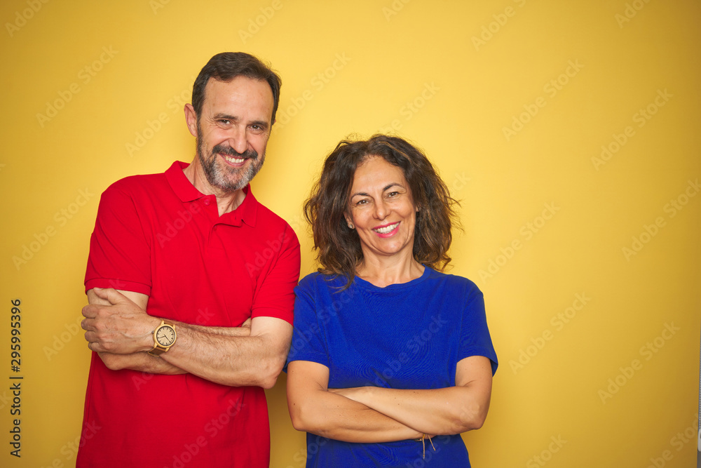 Beautiful middle age couple together standing over isolated yellow background happy face smiling with crossed arms looking at the camera. Positive person. Beautiful middle age couple together standing over isolated yellow background happy face smiling with crossed arms looking at the camera. Positive person.