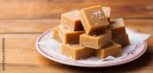 Caramel fudge candies on a plate. Wooden background. Close up.