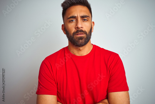Young indian man wearing red t-shirt over isolated white background skeptic and nervous, disapproving expression on face with crossed arms. Negative person.