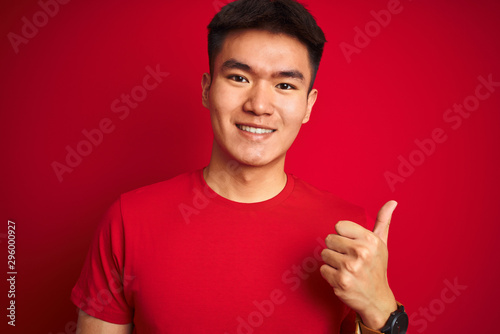 Young asian chinese man wearing  t-shirt standing over isolated red background happy with big smile doing ok sign, thumb up with fingers, excellent sign