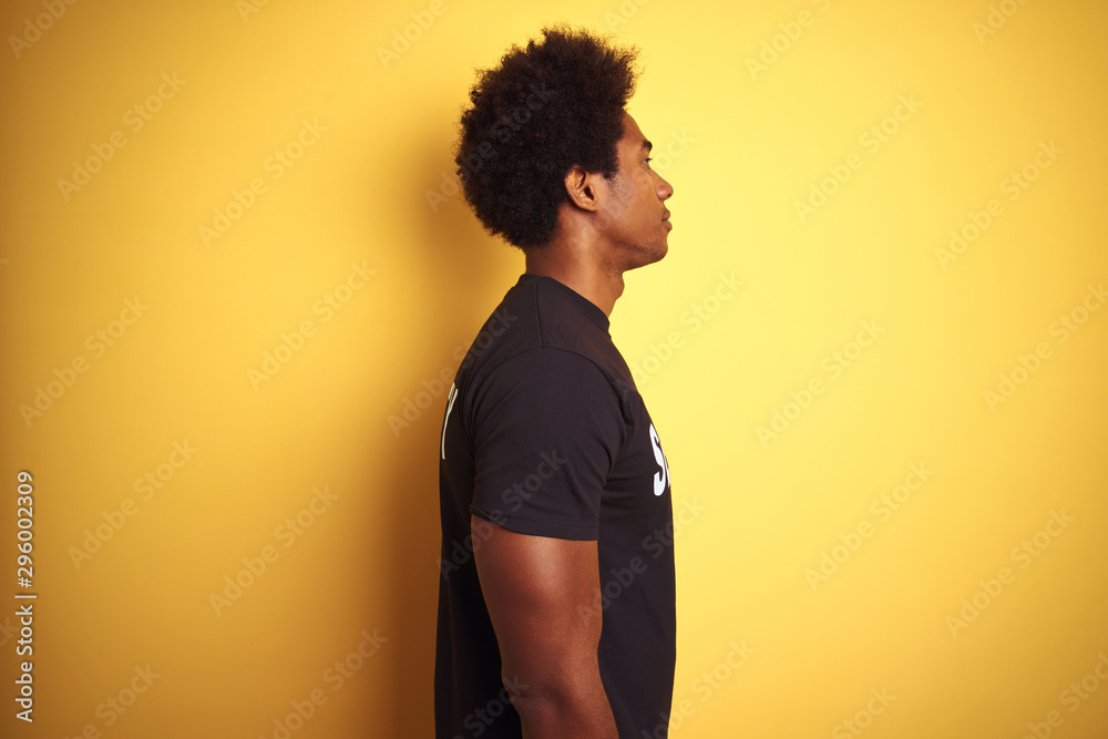 American safeguard man with afro hair wearing security uniform over isolated yellow background looking to side, relax profile pose with natural face with confident smile.