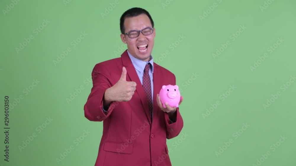 Happy Asian businessman with eyeglasses holding piggy bank and giving thumbs up Happy Asian businessman with eyeglasses holding piggy bank and giving thumbs up