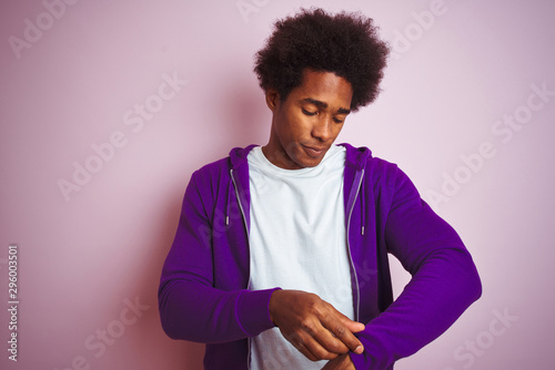Young african american man wearing purple sweatshirt standing over isolated pink background amazed and surprised looking up and pointing with fingers and raised arms. © Krakenimages.com
