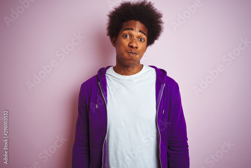 Young african american man wearing purple sweatshirt standing over isolated pink background puffing cheeks with funny face. Mouth inflated with air, crazy expression.
