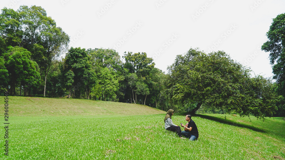 Asian muslim couple in love playing acoustic song guitar sitting on grass in the park under the tree Asian muslim couple in love playing acoustic song guitar sitting on grass in the park under the tree