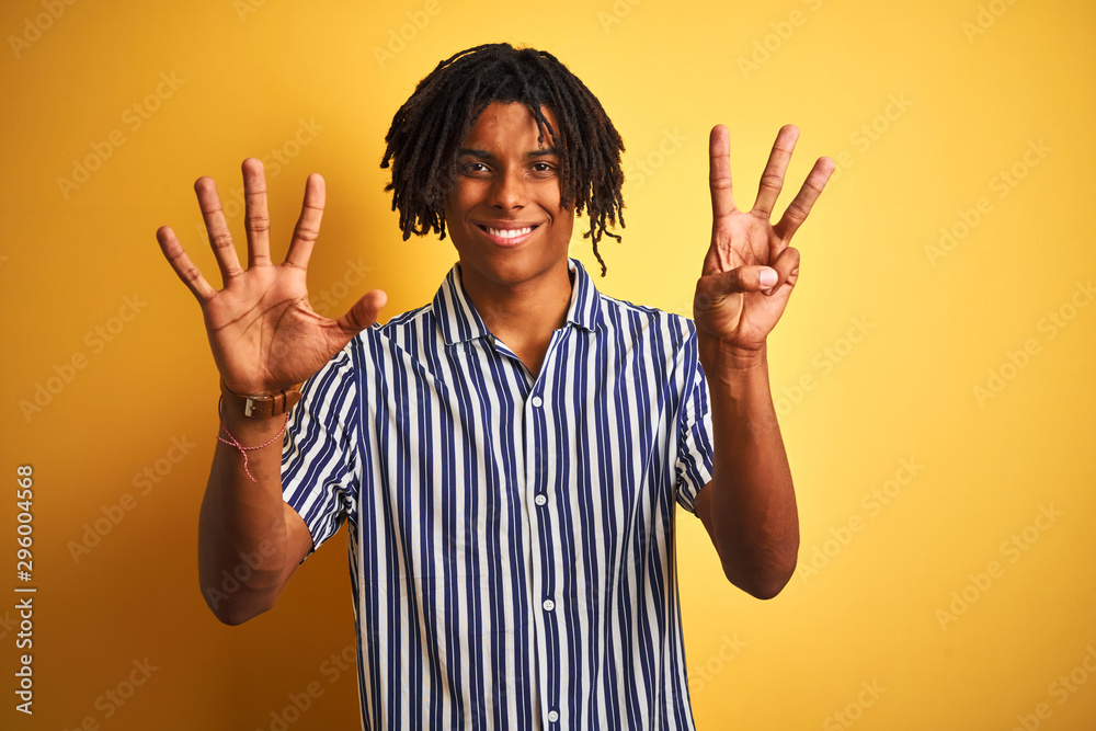 Afro man with dreadlocks wearing casual striped t-shirt over isolated yellow background showing and pointing up with fingers number eight while smiling confident and happy. Afro man with dreadlocks wearing casual striped t-shirt over isolated yellow background showing and pointing up with fingers number eight while smiling confident and happy.