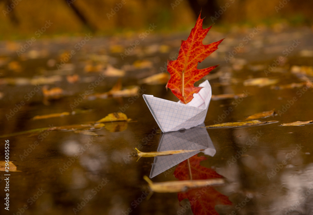 A paper boat floats in a puddle, instead of a sail it has a red