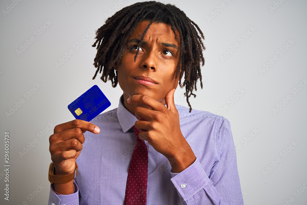 Afro american businessman with dreadlocks holding credit card over isolated white background serious face thinking about question, very confused idea