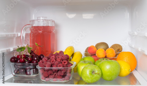 on the shelf of a white fridge, close-up, fresh fruit, berries and compote in a glass jug