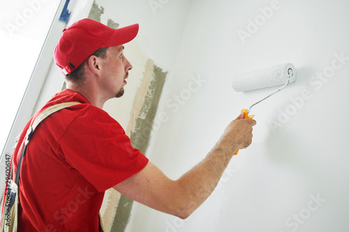 Fototapeta Naklejka Na Ścianę i Meble -  Painter worker with roller painting wall surface into white